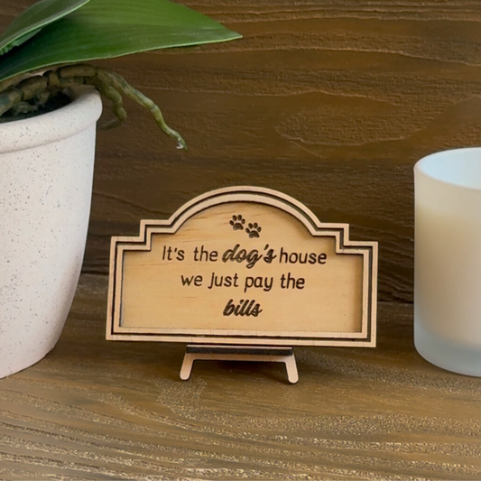 Cute Miniature Pine Plywood sign with easel stand featuring a laser engraved quote "It's the Dog's House, we just pay the Bills" Approx 6cm High and 10cm Wide. 